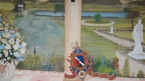 Ein Wandgemälde mit einer Landschaft, eine Säule mit einem Wappen und eine Statue.