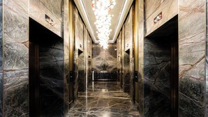 Un corridoio in marmo con lampadario, ascensori e una parete decorativa centrale.
