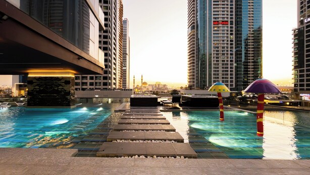 Una piscina sul tetto con acqua cristallina, circondata da edifici alti e un tramonto sullo sfondo.