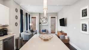 A modern kitchen with a central island, a dining area with a sofa, and a TV mounted on the wall. - Skyline Haven #1–Nashville Views–Sleeps 6 (Nashville)