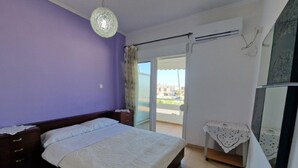 Et soveværelse med seng, natbord, kommode, loftlampe, et vindue med gardiner og en balkonudgang.