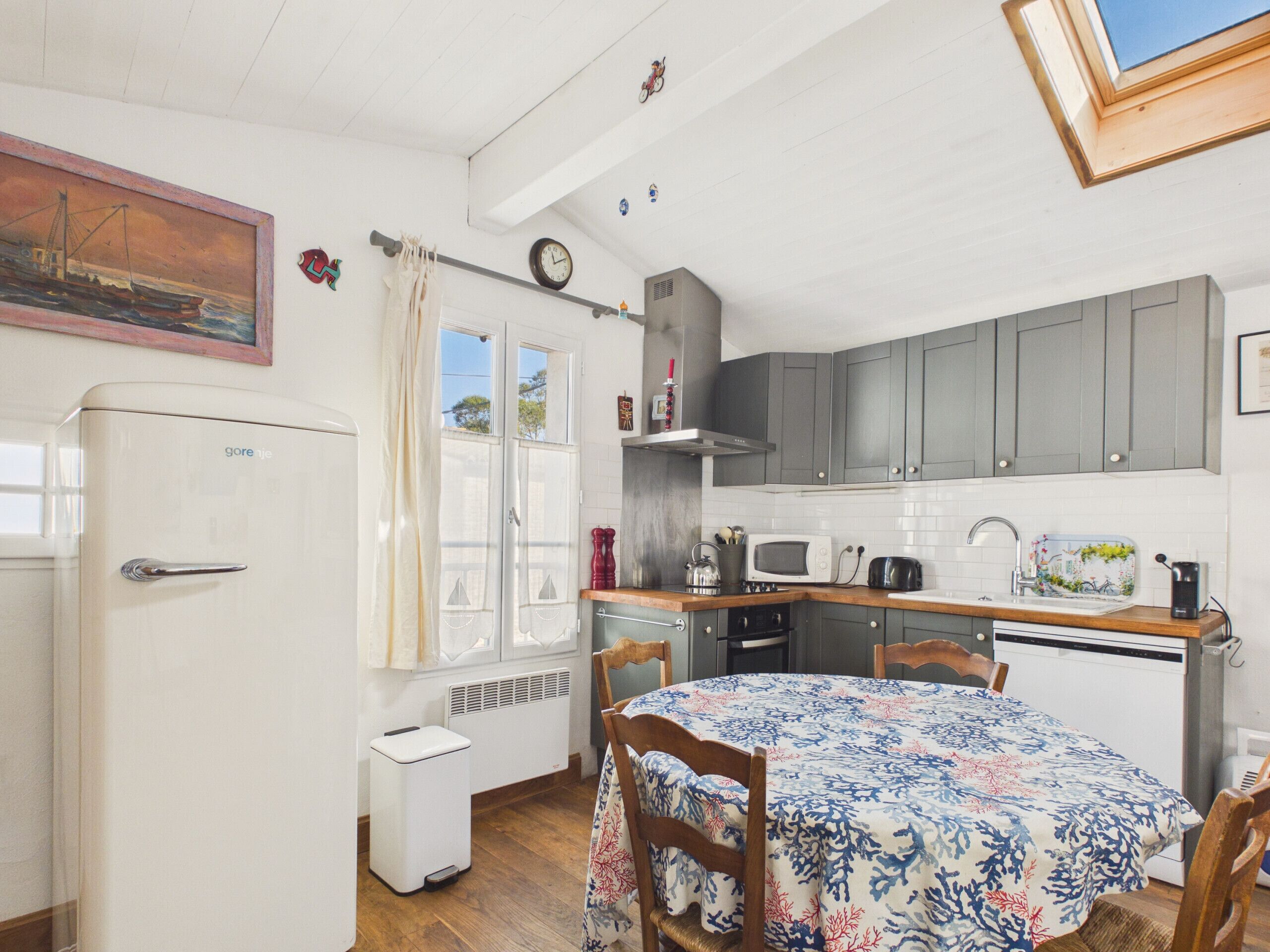 A compact kitchen with a refrigerator, stove, microwave, and sink. There is a dining table with chairs and a window with curtains.