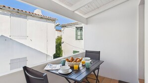 Een balkon met een ontbijttafel, compleet met croissants, een krant en sinaasappelsap.