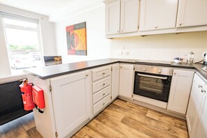 A kitchen with white cabinets, a black countertop, a wooden floor, and a window with a view of parked cars. - Modern 2-Bedroom Galway City Apartment (Galway)