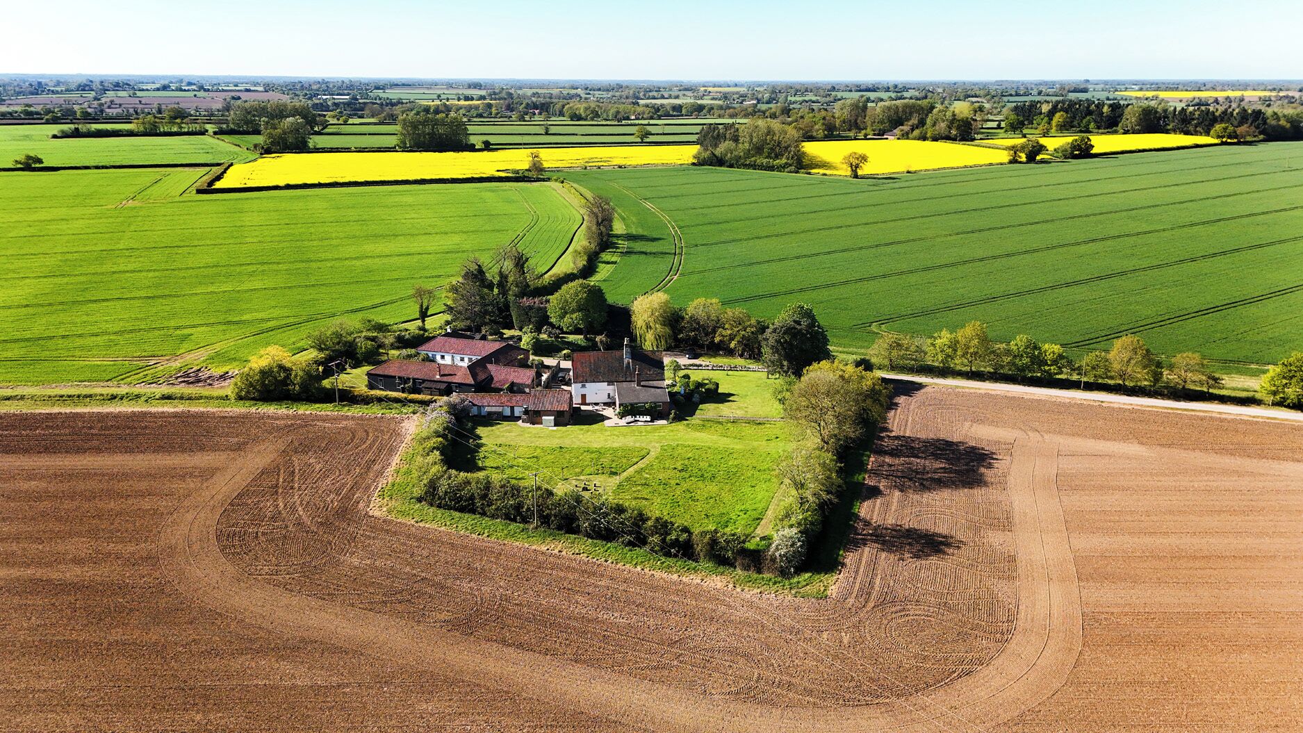 An aerial view of a rural property with fields, a farmhouse, and surrounding greenery.