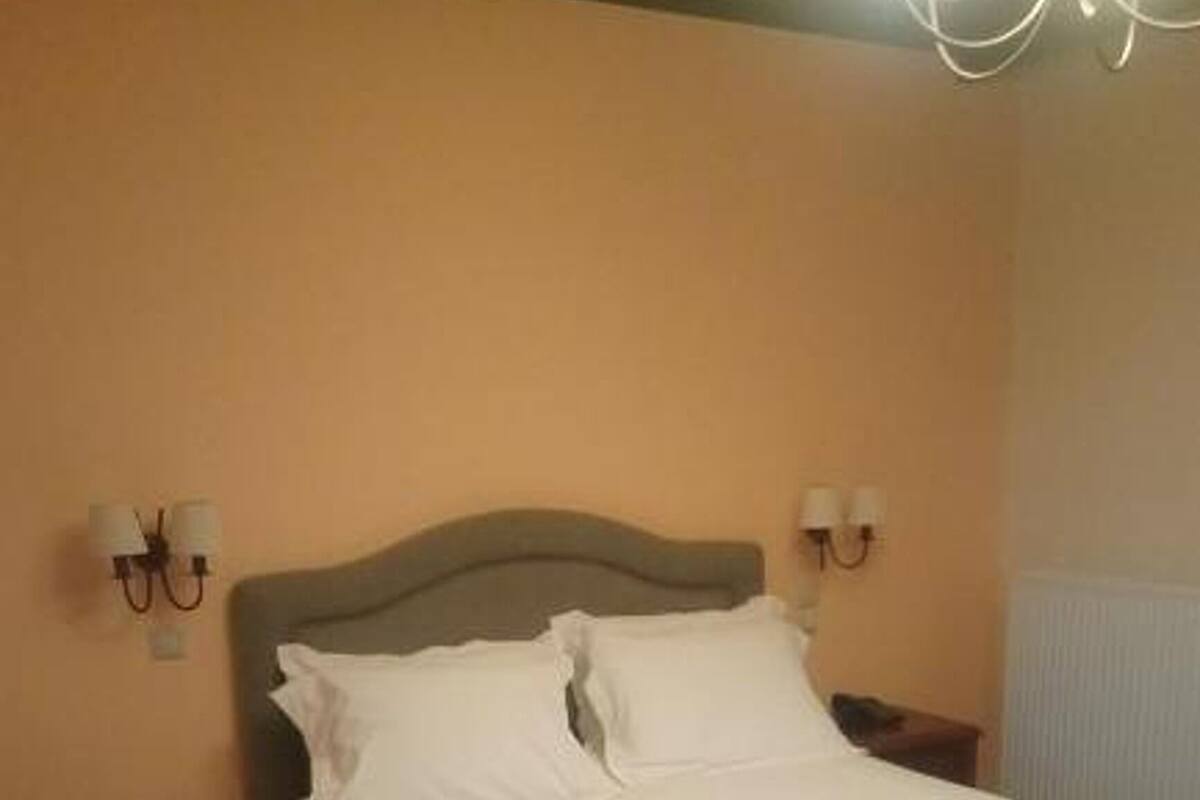A neatly made bed with white linens and a striped blanket, a wooden floor, and a simple nightstand with a lamp.