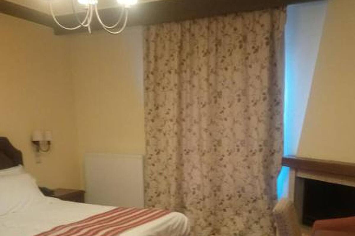 A bedroom with a bed, a nightstand, a dresser, a window with curtains, and a chandelier.