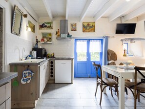 Une cuisine avec une porte bleue, des carreaux blancs et un coin repas avec des chaises en bois.