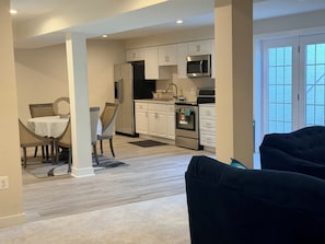 A modern kitchen with white cabinets, a microwave, and an oven. There is a dining area with a table and chairs, and a dark-colored sofa in the foreground. - Serene 1-bedroom basement in welcoming Upper Marlboro perfect for getaway (Upper Marlboro)