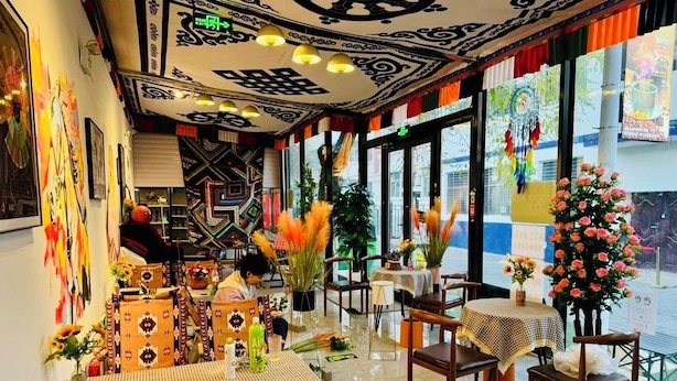 Un ristorante con interni moderni, caratterizzato da un mix di arredo tradizionale e contemporaneo, tra cui pareti decorate, ampie finestre e diversi tipi di tavoli.