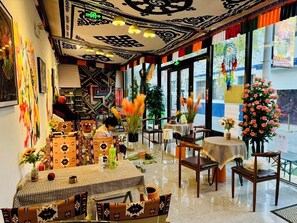 Ein Restaurant mit modernem Interieur, das eine Mischung aus traditioneller und zeitgenössischer Dekoration zeigt, darunter gemusterte Wände, große Fenster und verschiedene Tischgestaltungen.