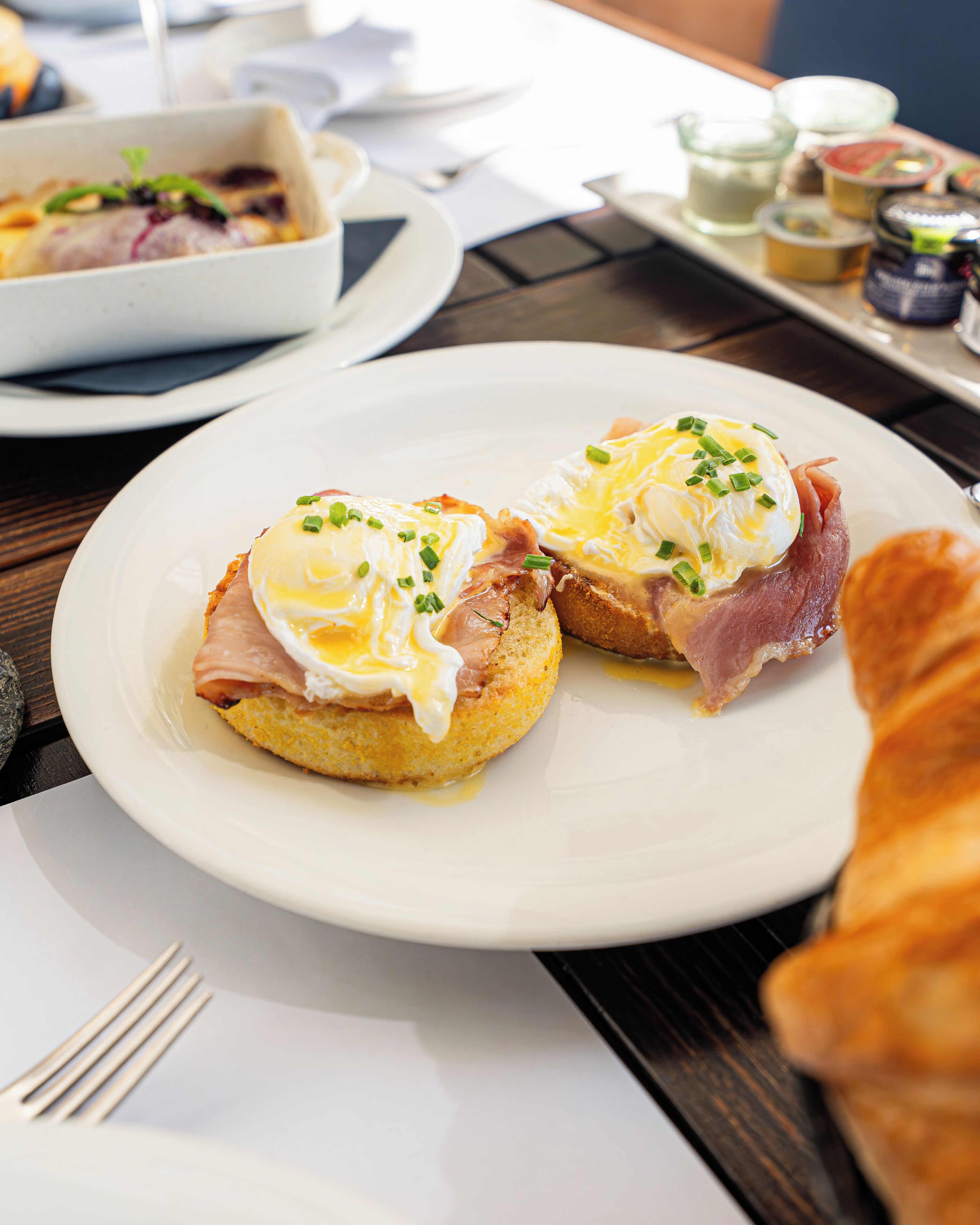 Ein Frühstückstisch mit Eggs Benedict auf einem Teller, einem Croissant und einer kleinen Schale mit Beilagen.