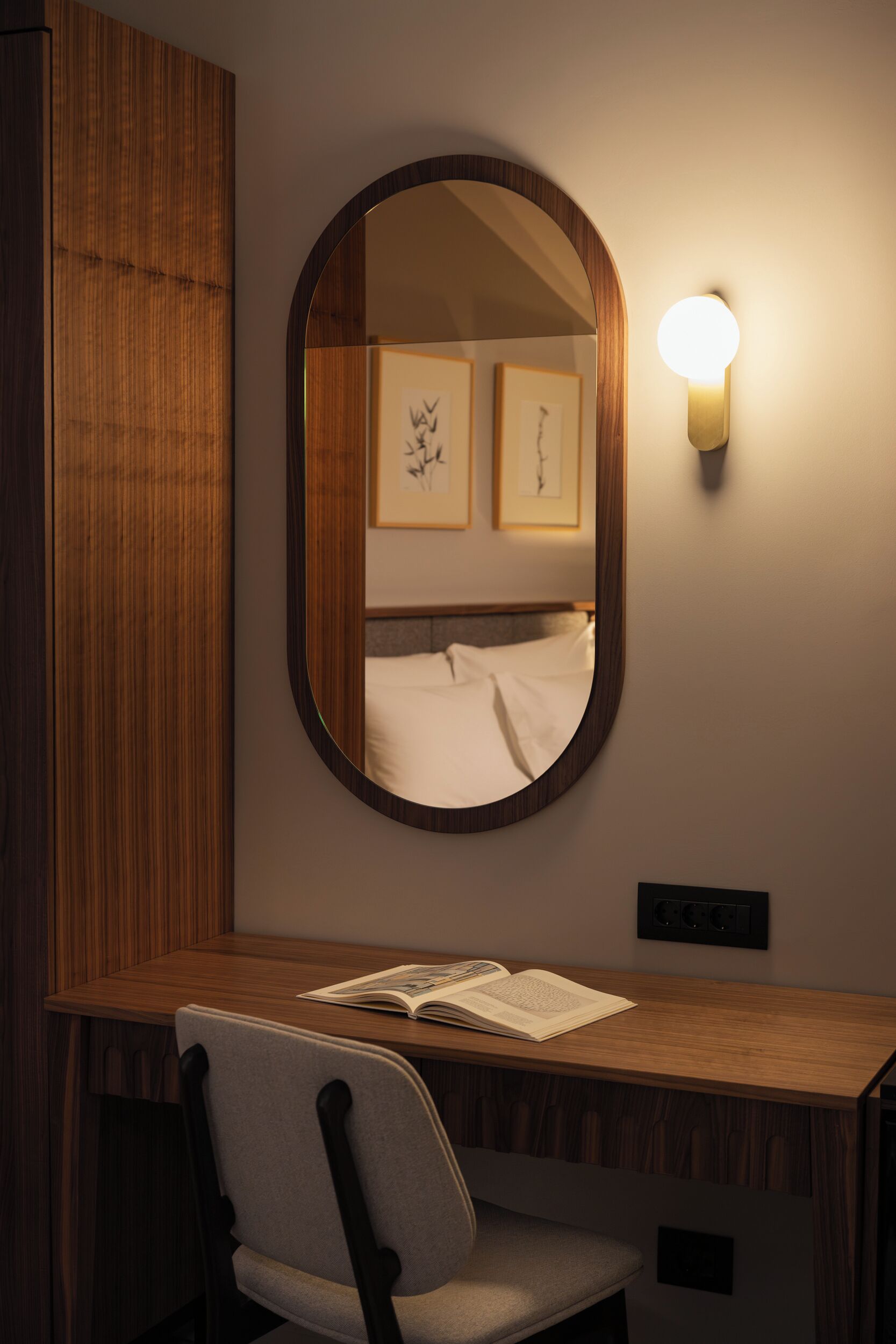Ein Hotelzimmer mit einem Holztisch, einem Stuhl, einem Nachttisch, einem Spiegel und einer Wandleuchte.