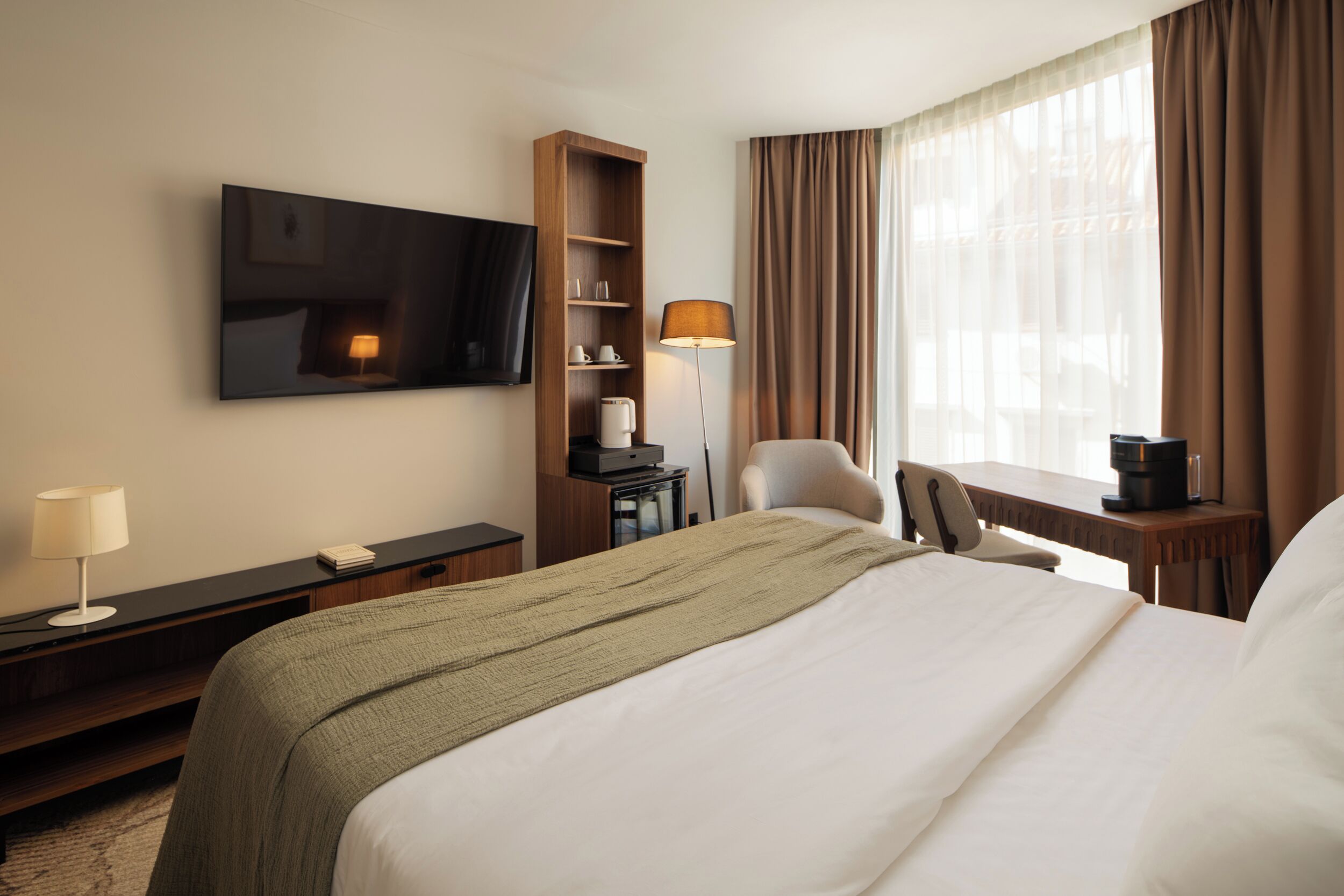 Une chambre d’hôtel équipée d’un lit, d’un téléviseur fixé au mur, d’un bureau avec une lampe, d’une chaise et d’une machine à café.