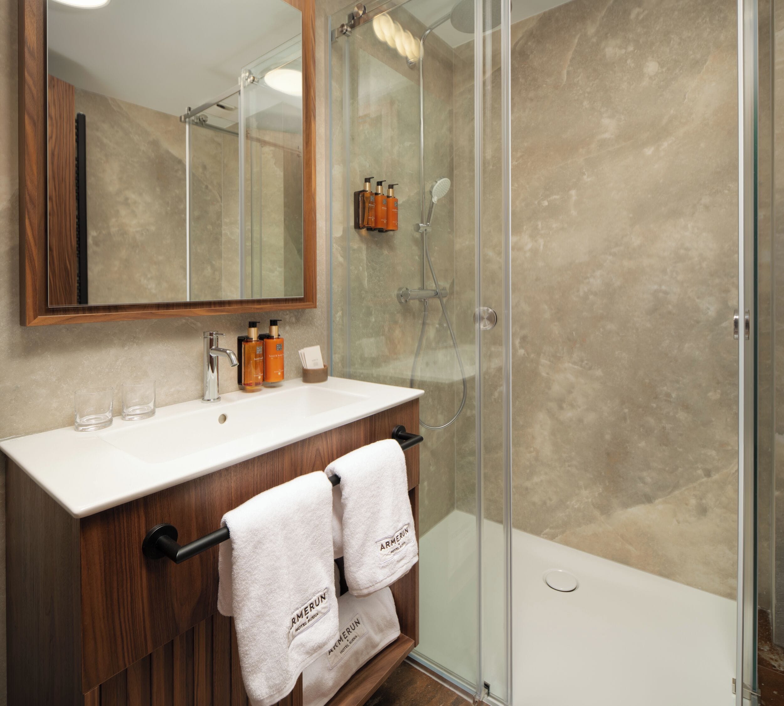 A bathroom with a glass-enclosed shower, a wooden vanity with a mirror, and two towels hanging on a rack.
