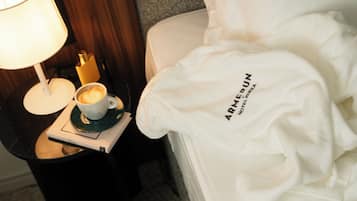A hotel room with a bed, a nightstand with a lamp, a cup of coffee, and a pair of slippers.