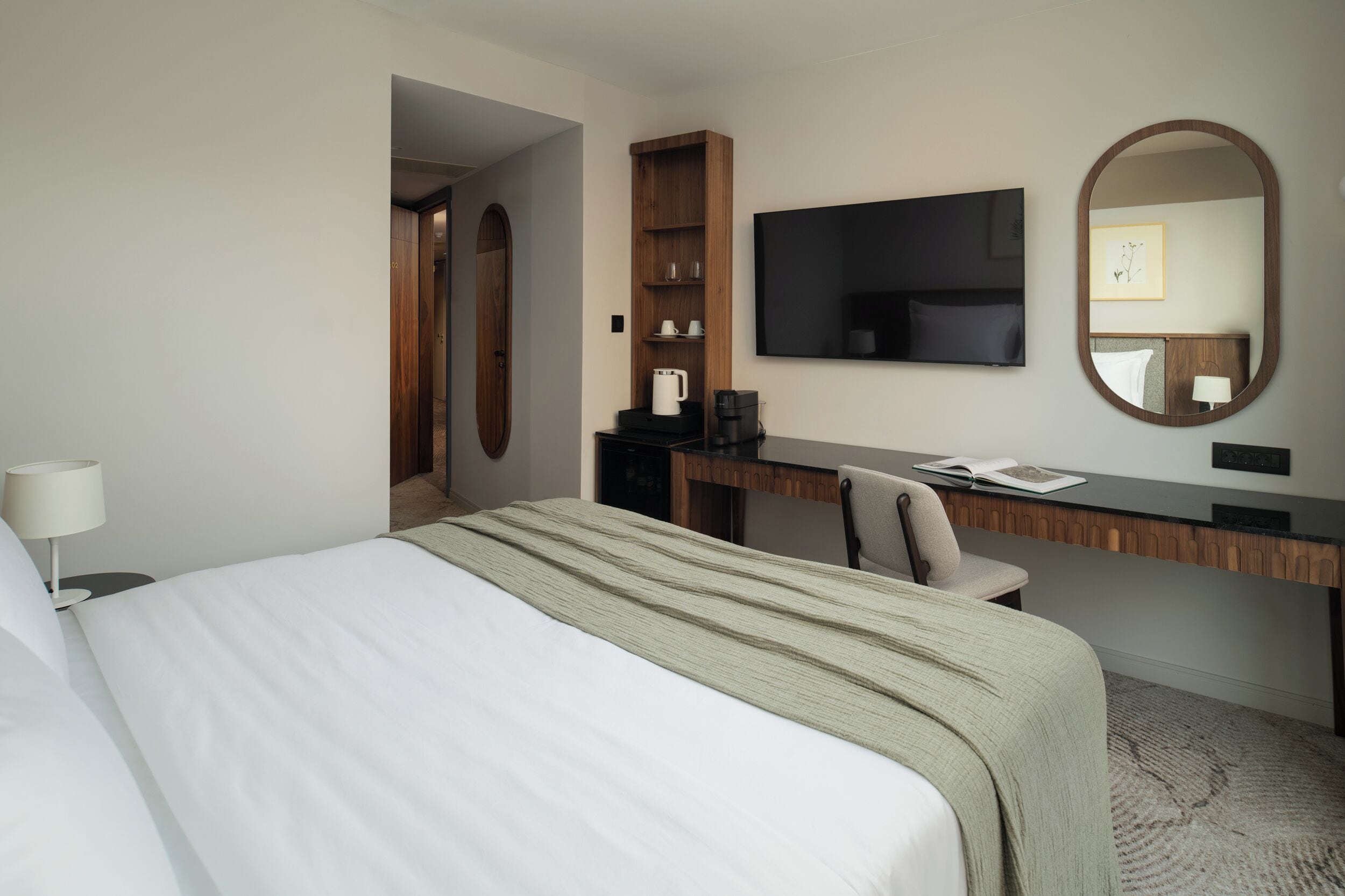 Una habitación de hotel con una cama, un escritorio, una silla, un televisor y un espejo.