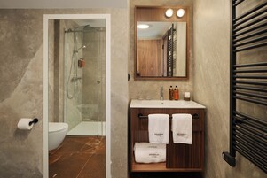 A bathroom with a glass shower enclosure, a toilet, a sink with a wooden vanity, and a towel rack with towels.