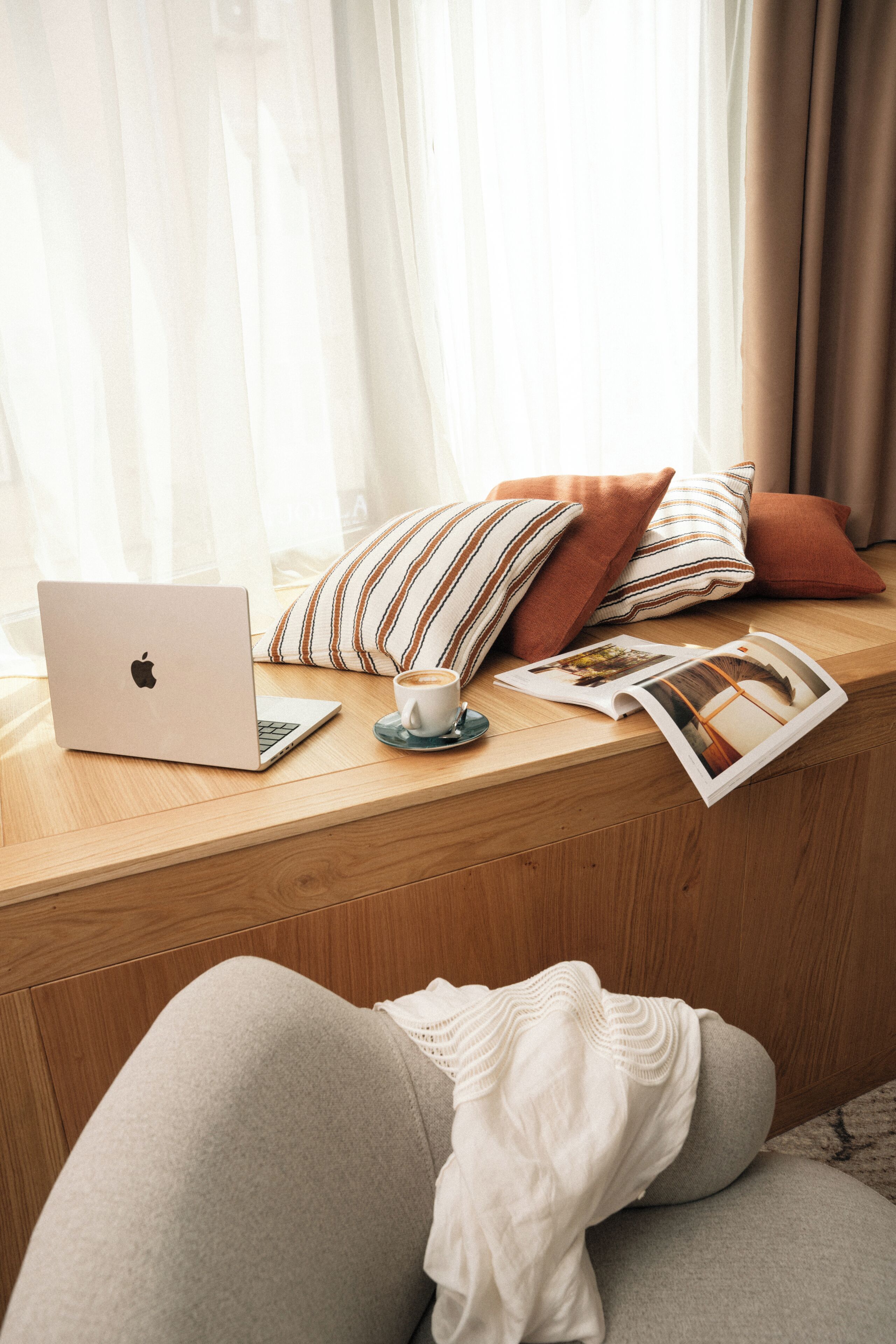 A laptop on a wooden surface, a cup, and a magazine.