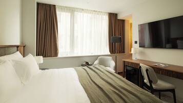 A hotel room with a bed, a desk, a chair, a TV, and a window with curtains.