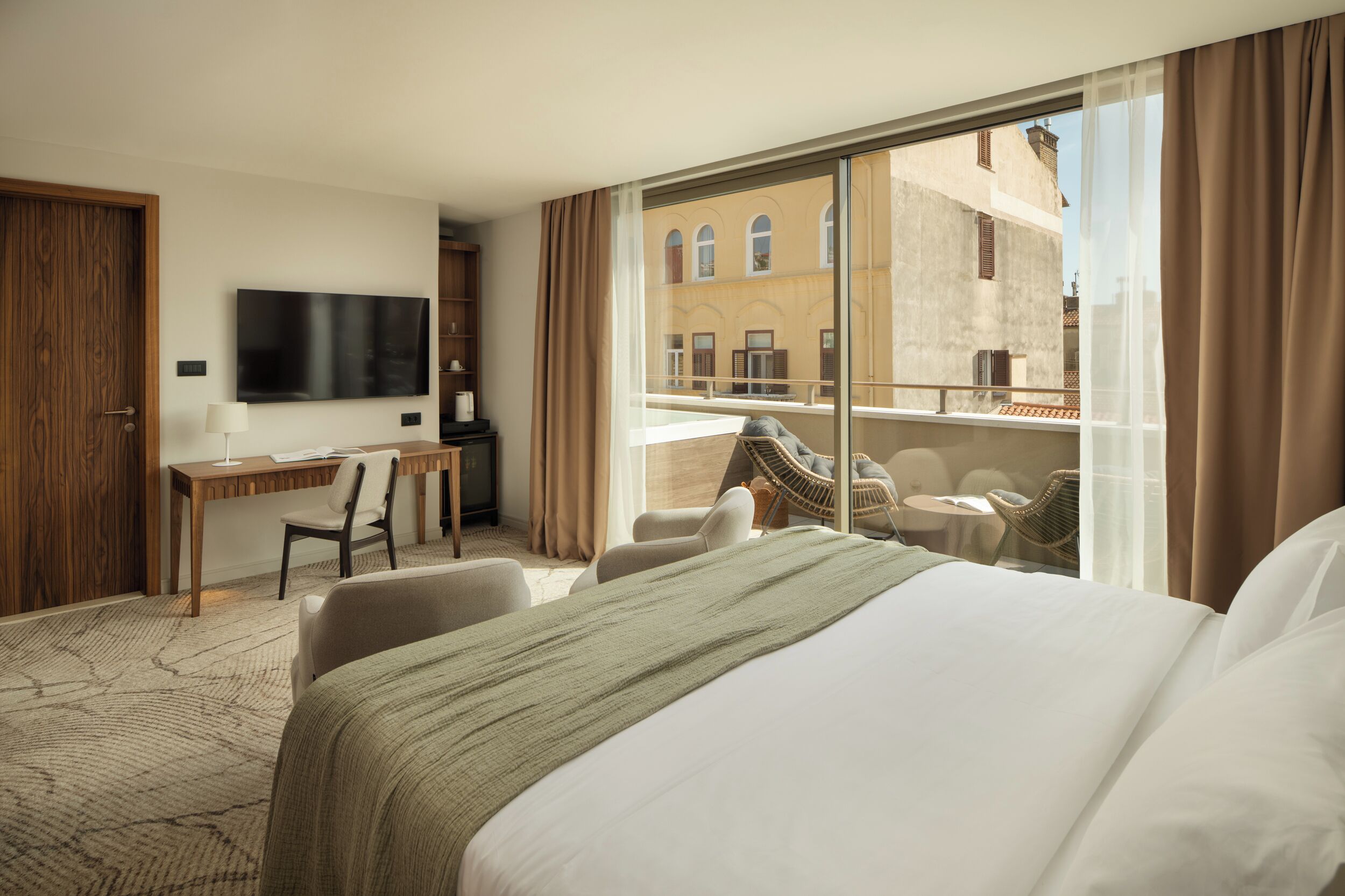 Habitación de hotel con cama, escritorio, televisión y balcón con asientos.