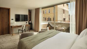 A hotel room with a bed, desk, TV, and a balcony with seating.