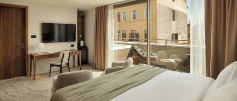 Habitación de hotel con cama, escritorio, televisión y balcón con asientos.