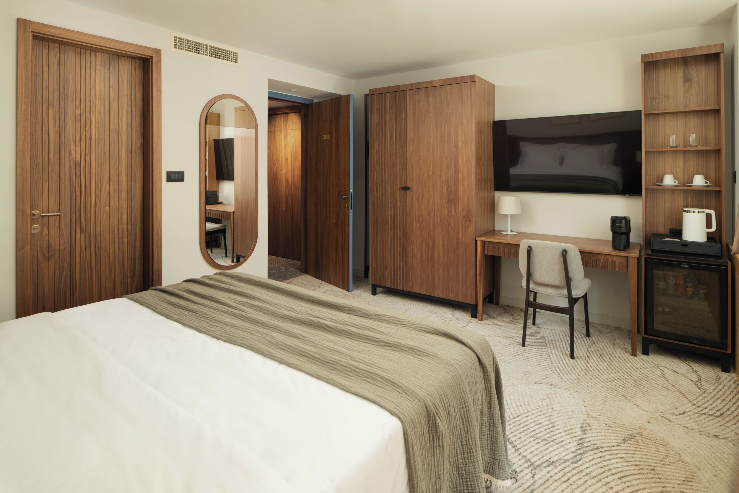 A hotel room with a bed, a desk, a chair, a television, and a wardrobe.