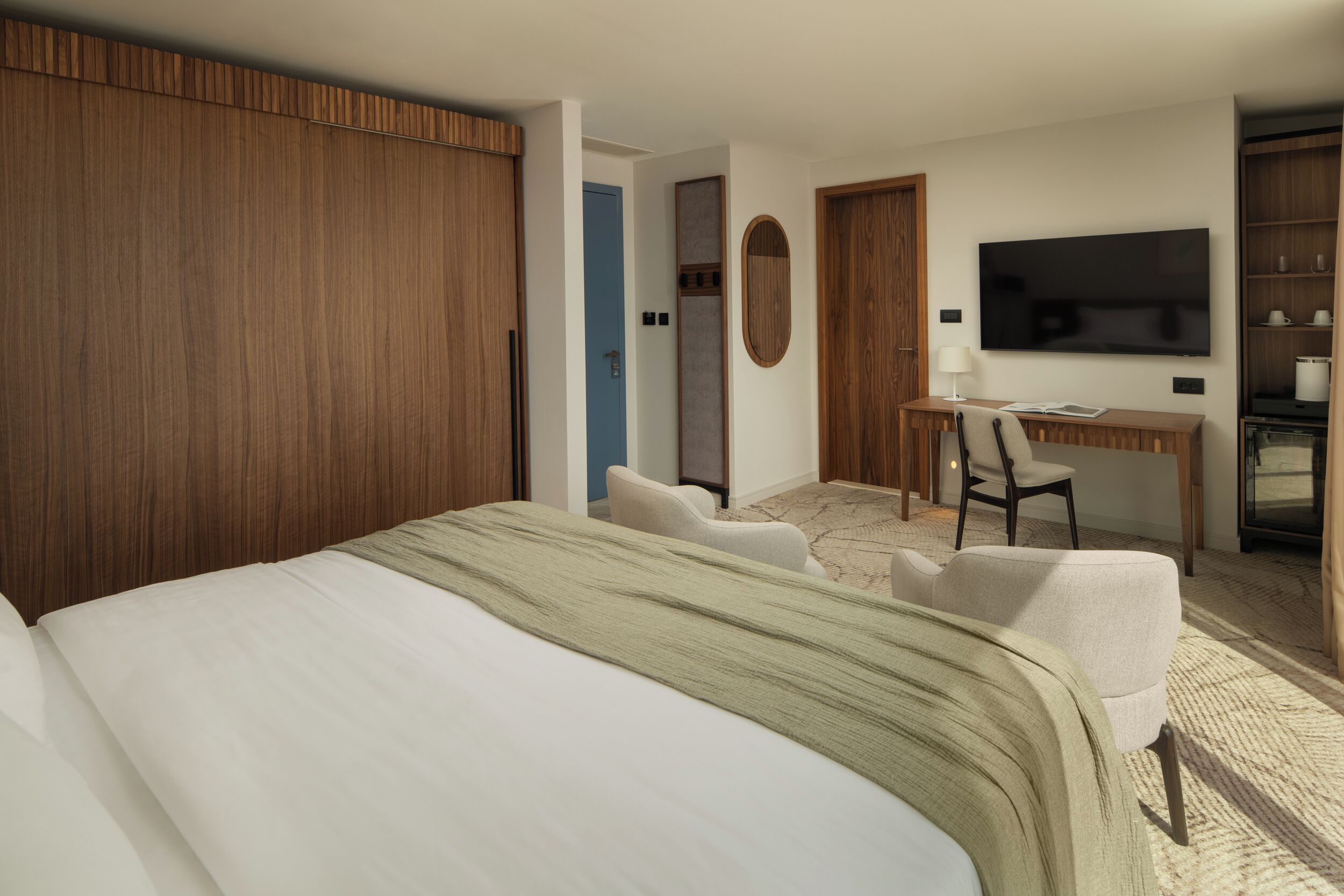 Quarto de hotel com cama, escrivaninha, televisão e guarda-roupa.