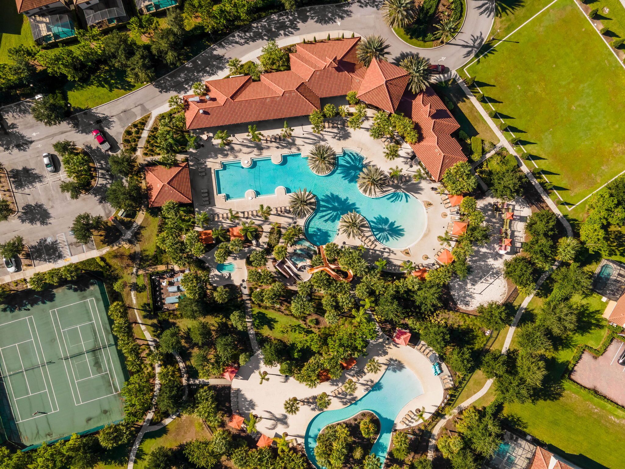 An aerial view of a resort with multiple swimming pools, tennis courts, and lush landscaping.