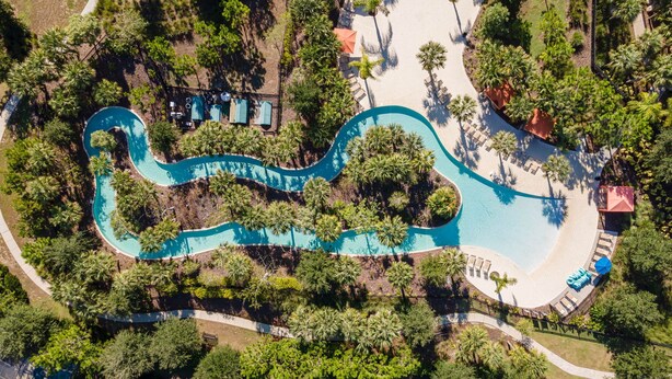 Vista aérea de un resort con piscina sinuosa, palmeras y tumbonas.