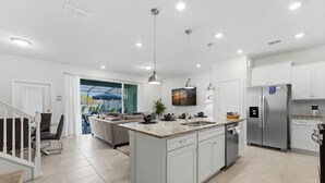 Una cocina moderna con armarios blancos, una isla central, electrodomésticos de acero inoxidable e iluminación colgante.