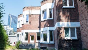Een rij herenhuisjes van baksteen met witte raamkozijnen, een zichtbare bakstenen schoorsteen en een ladder op het dak.