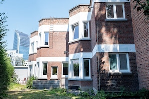 A row of brick townhouses with white window frames, a visible brick chimney, and a ladder on the roof. - Cool Cool House (Liège)