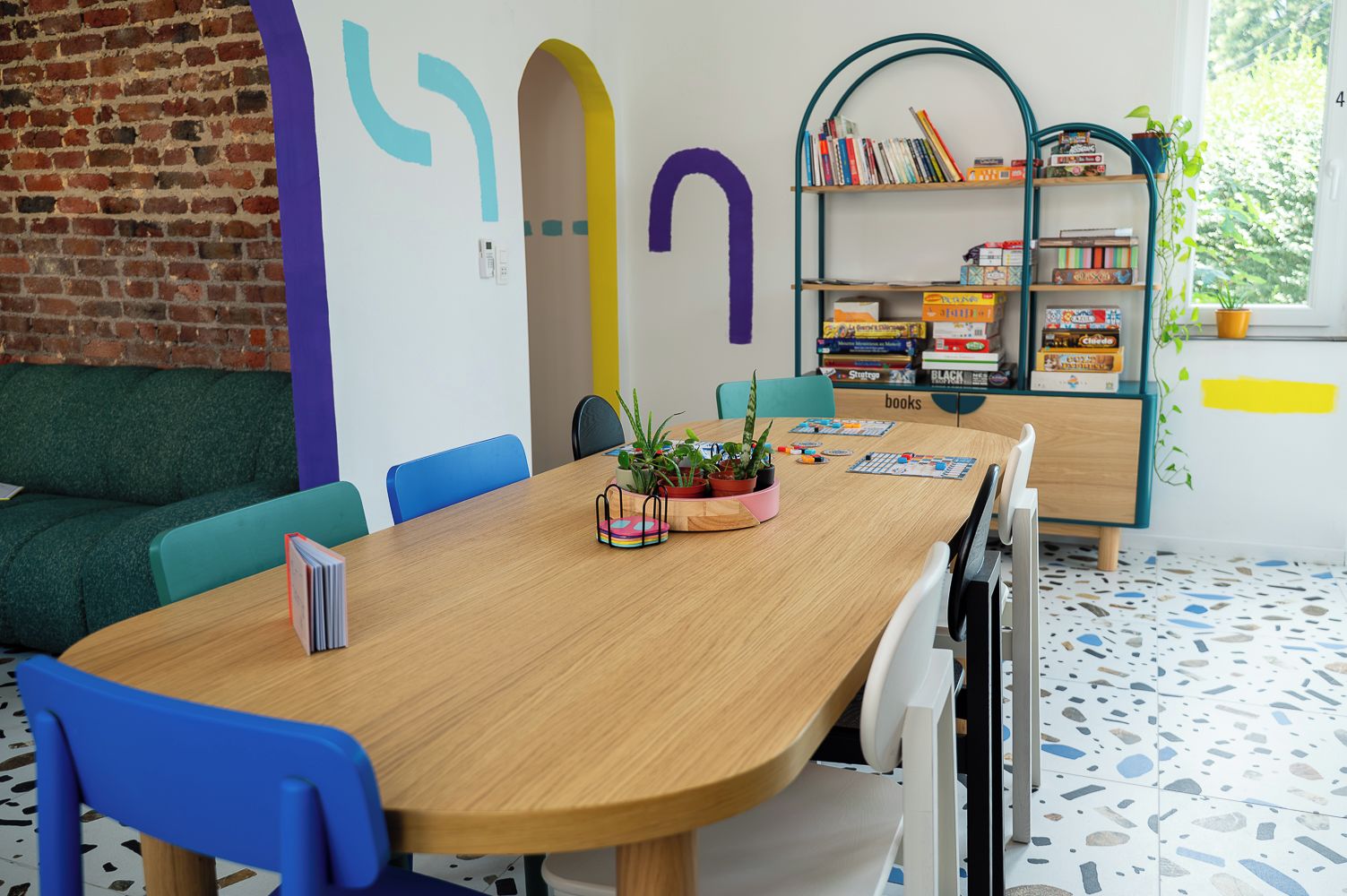Een gezellige kamer met een houten tafel, blauwe stoelen, een boekenkast en een bakstenen muur.