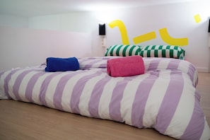 Ein Bett mit gestreifter Bettwäsche und zwei aufgerollten Handtüchern, eine Wand mit einem gelben abstrakten Design und ein Holzboden.