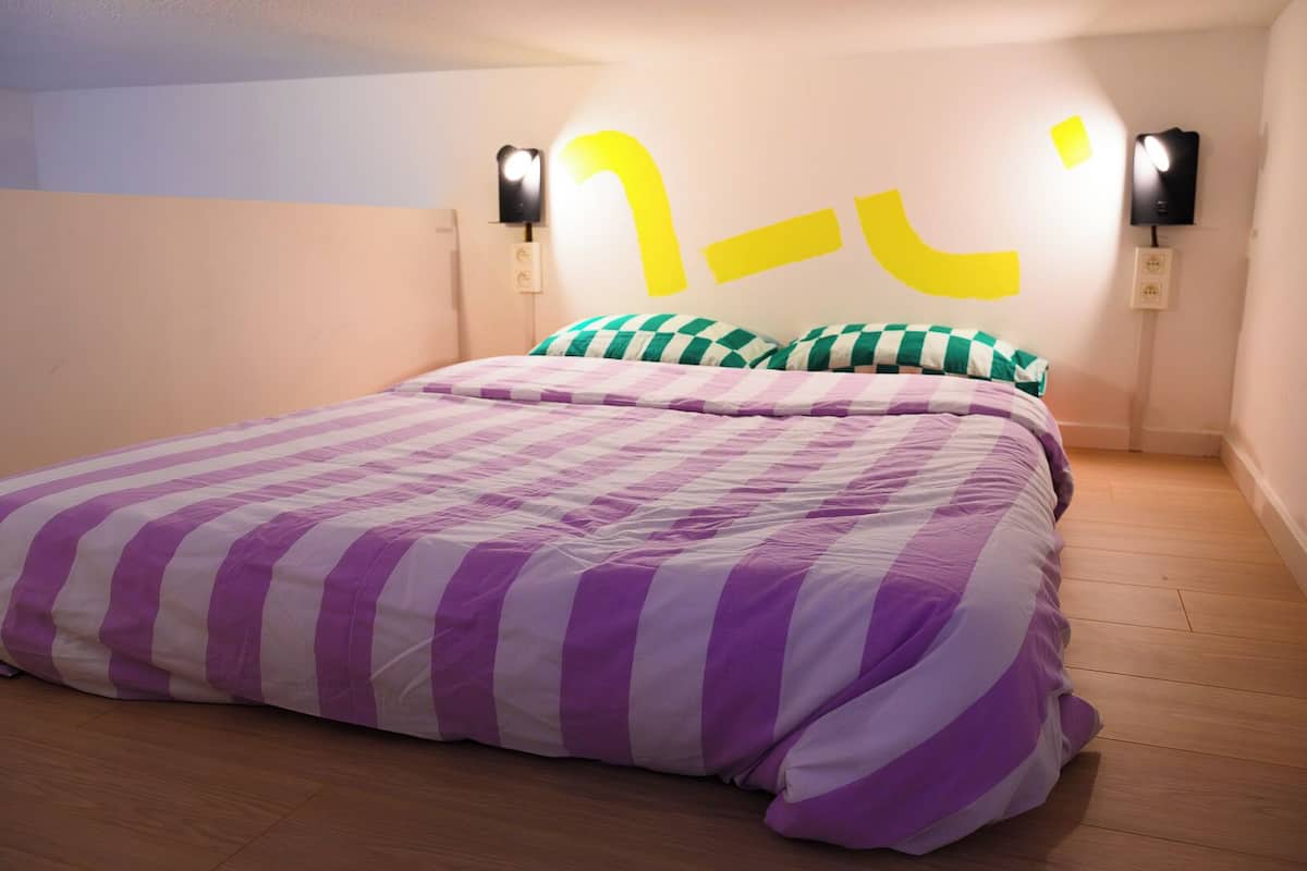 A bedroom with a large bed, striped bedding, and two wall-mounted light fixtures.