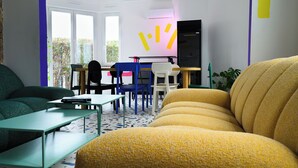 A modern living room with a green sofa, a yellow sofa, a small table, and a chair. There is a desk with a computer and a chair in the background. - Cool Cool House (Liège)