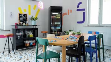Een modern interieur met een houten tafel, kleurrijke stoelen, een zwarte boekenkast en een neonbord.