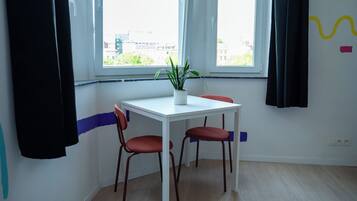 Une pièce avec une table blanche, deux chaises rouges, une plante en pot et une fenêtre avec des rideaux.