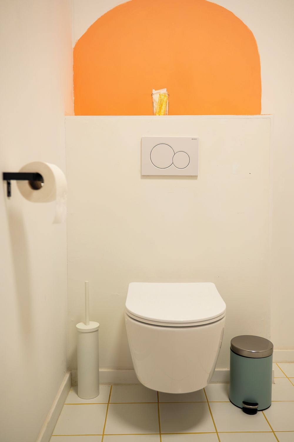 Un baño con inodoro, un cubo de basura y un dispensador de papel higiénico.
