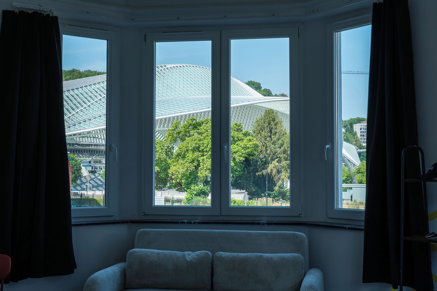 Une pièce dotée d’une baie vitrée donnant sur un bâtiment moderne à la façade en verre, entouré d’arbres.