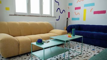 Een kamer met een gele bank, een blauwe bank, een glazen salontafel en een kamer met een patroon vloer.