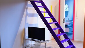 A modern living room with a wooden ceiling, a TV on a metal stand, a sofa, and a purple ladder. - Cool Cool House (Liège)