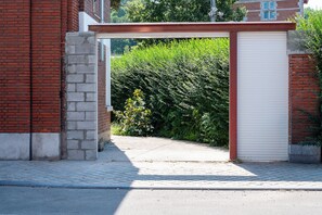 A gated entrance with a metal gate, a brick wall, and a white garage door. - Cool Cool House (Liège)