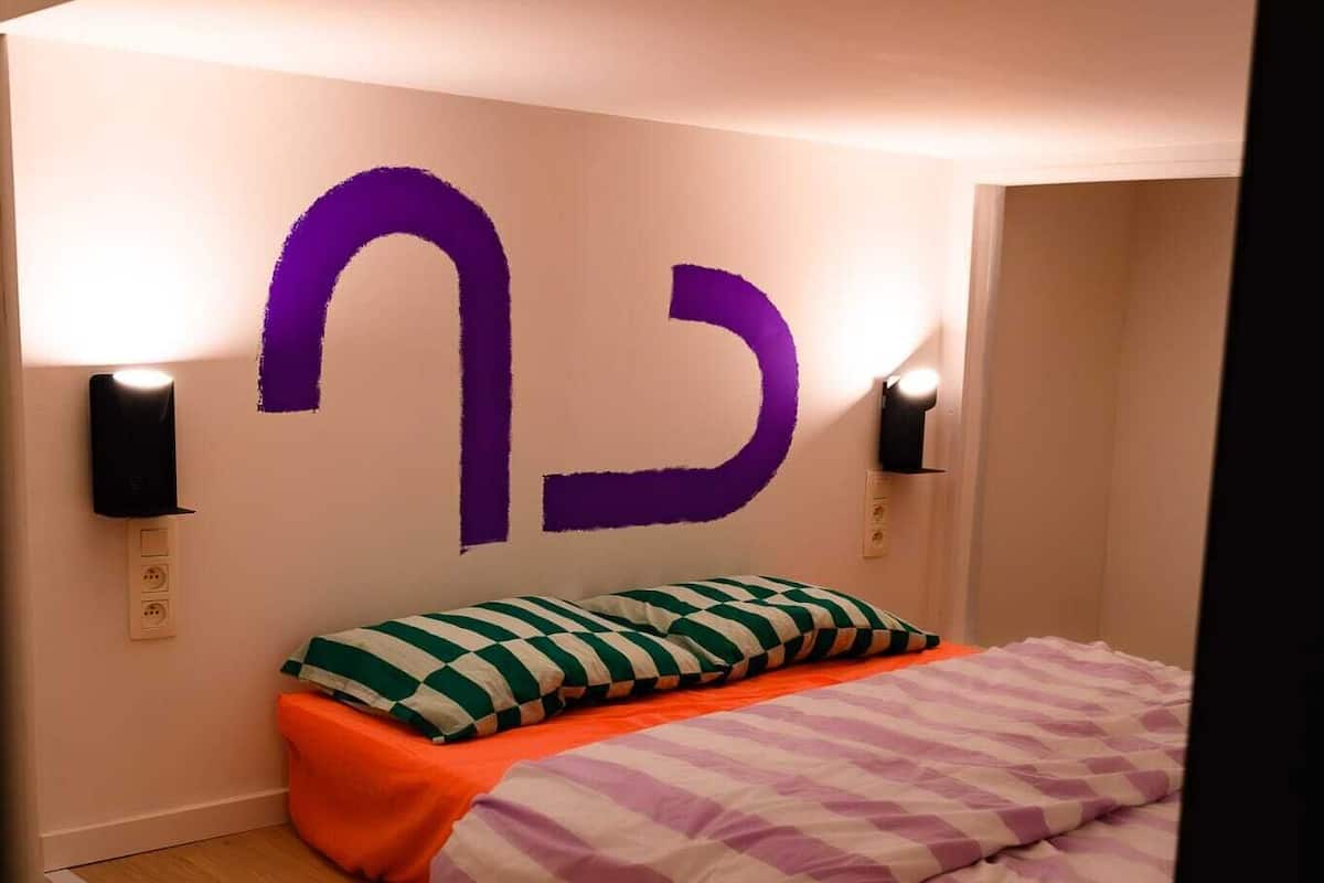 A room with a bed, a wall-mounted light fixture, and a wall decoration.