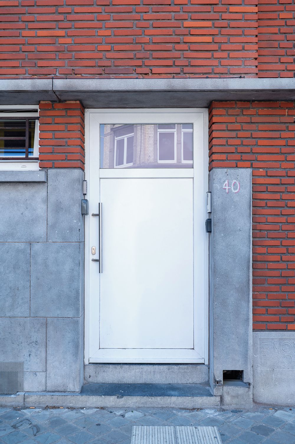 Eine weiße Tür mit einem kleinen Fenster darüber, in eine Ziegelwand eingelassen, mit der Nummer 40 auf der rechten Seite.