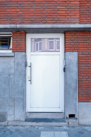 Eine weiße Tür mit einem kleinen Fenster darüber, in eine Ziegelwand eingelassen, mit der Nummer 40 auf der rechten Seite.
