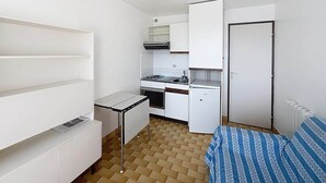 Ein kleines Zimmer mit Küchenzeile, einem Bett mit gestreifter Bettwäsche und einem weißen Kleiderschrank.