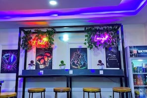 Eine Barbereich mit Neonreklamen mit den Aufschriften 'St. Paul' und 'Lounge', Barhocker und gerahmten Kunstwerken an der Wand.
